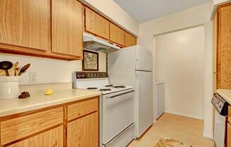 A compact kitchen here at High Plains with warm wood cabinets, light countertops, and white appliances, including a stove and refrigerator, offering a simple, functional layout with a clean and cozy feel.