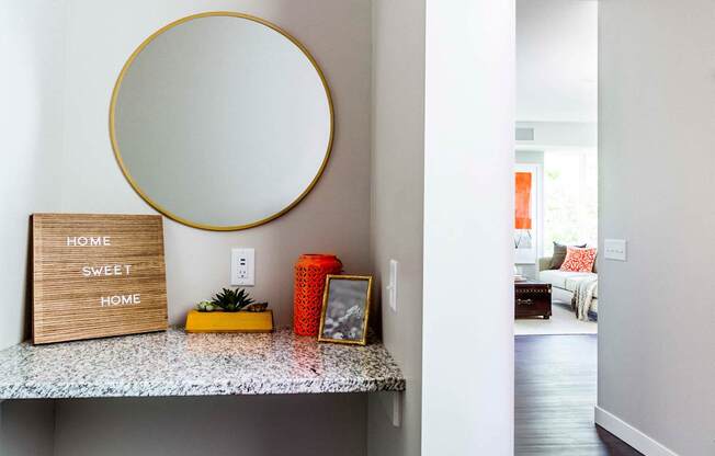 Entrance to a modern apartment: A sleek hallway vanity with a granite countertop welcomes guests, seamlessly transitioning into the well-lit living room flooded with natural light.