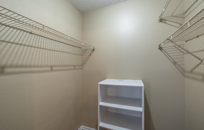 A white shelf unit with three shelves is in a room with white walls.