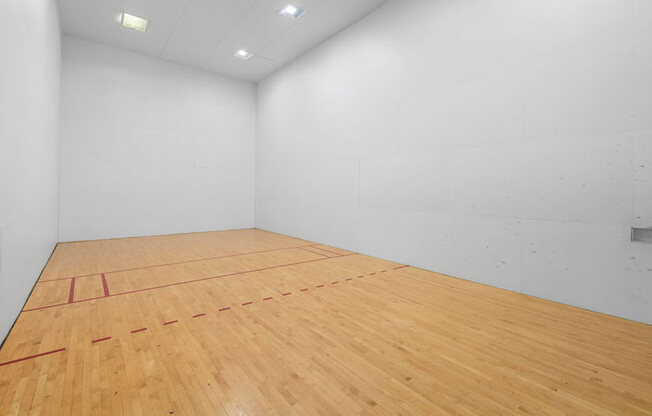 A squash court with a wooden floor and white walls.