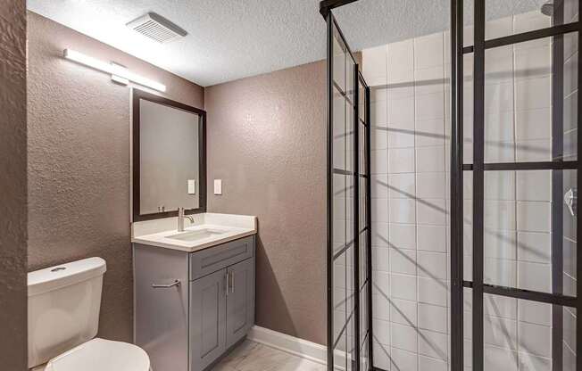 A bathroom with a white toilet, a sink with a cabinet and a shower with a glass door.