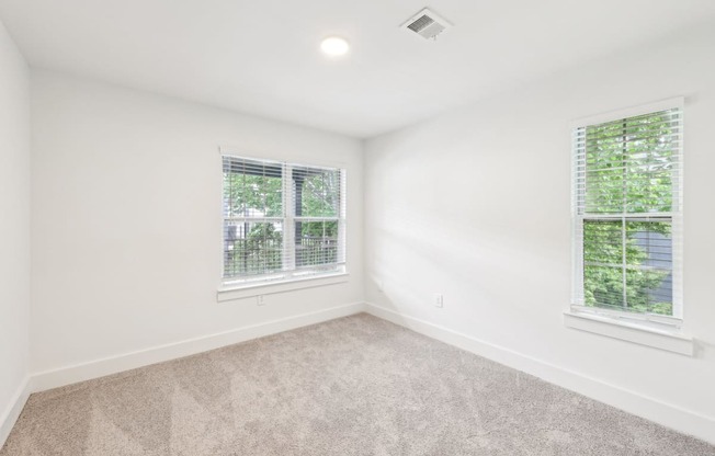 A bed room with a carpeted floor and two windows.