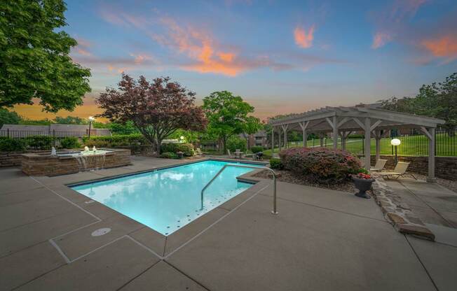 A swimming pool surrounded by a concrete patio and a stone wall with a fountain.