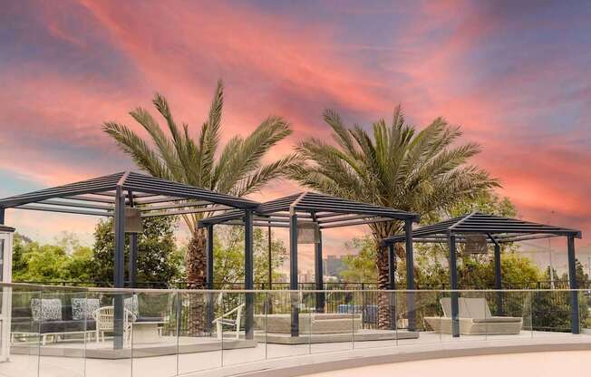 A patio area with a glass railing and a roof with palm trees in the background.