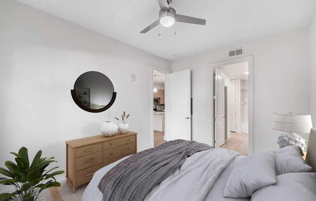 A bedroom with a bed, dresser, mirror, and plant.