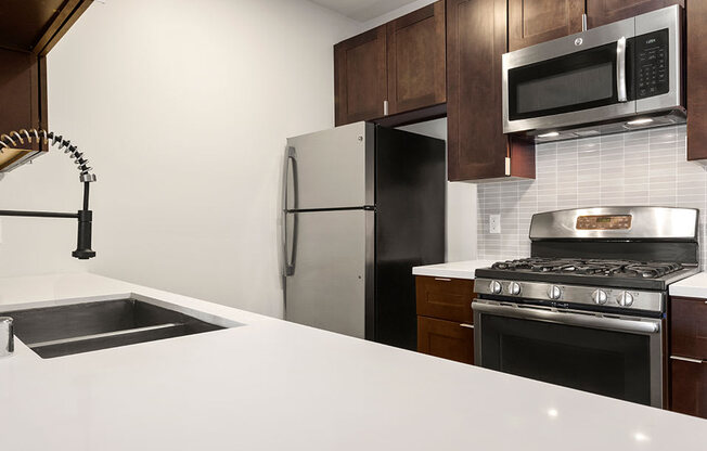 White tiled kitchen with modern faucet, stainless steel appliances, and refrigerator.