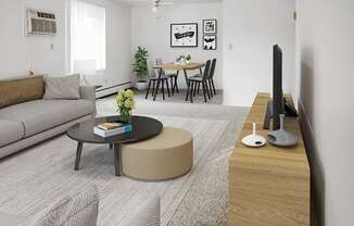 A living room with a grey sofa, a black coffee table, a round ottoman, a wooden TV stand, and a dining table with chairs.