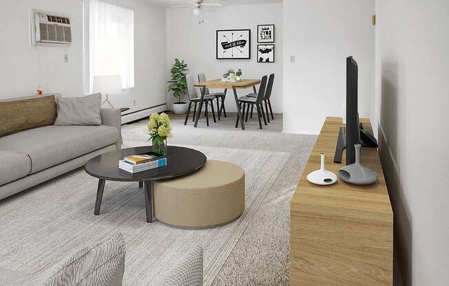 A living room with a grey sofa, a black coffee table, a round ottoman, a wooden TV stand, and a dining table with chairs.