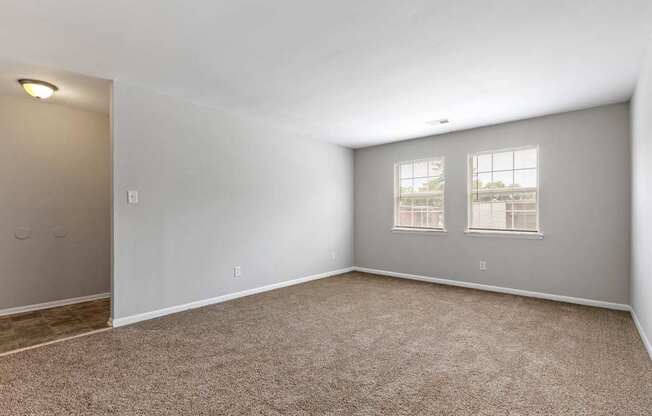 an empty living room with carpet and two windows