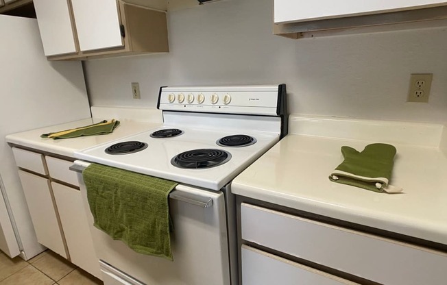 Kitchen with tile flooring featuring white cabinets, white appliances, white countertop, and green hand towel and oven mitt