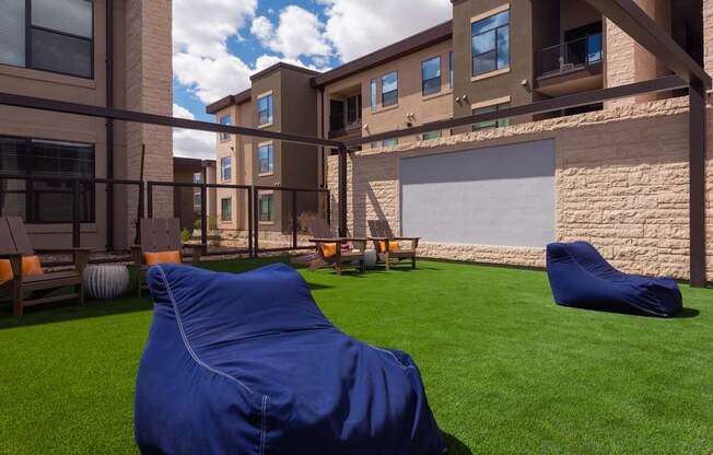 A blue bean bag chair sits on a lawn in front of a building.