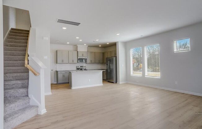 an empty living room and kitchen with a staircase in the background