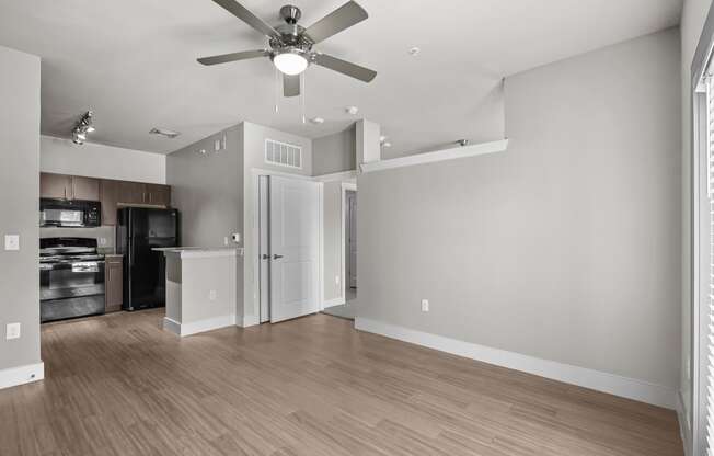 an empty living room with a ceiling fan and a kitchen