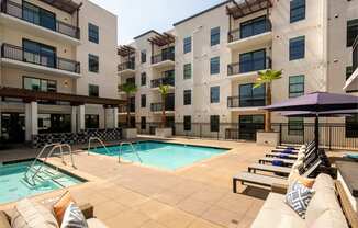 A pool area with a row of lounge chairs and a purple umbrella.