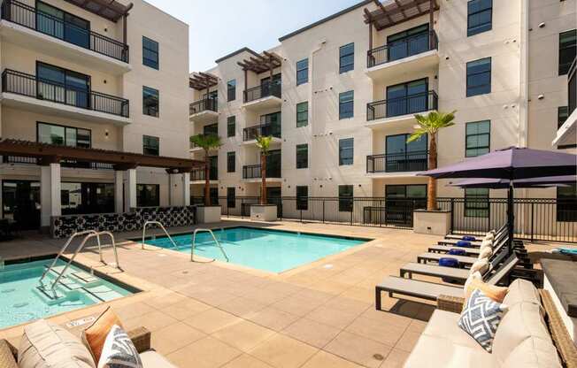 A pool area with a row of lounge chairs and a purple umbrella.