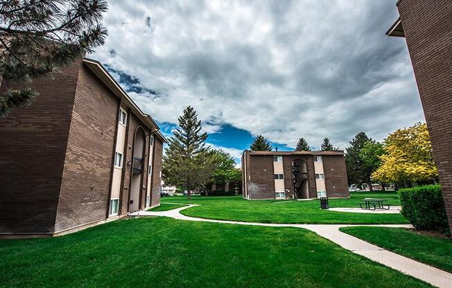 A grassy area with a pathway and two buildings on either side.