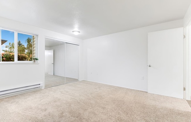 a spacious living room with white walls and carpeting and a large window