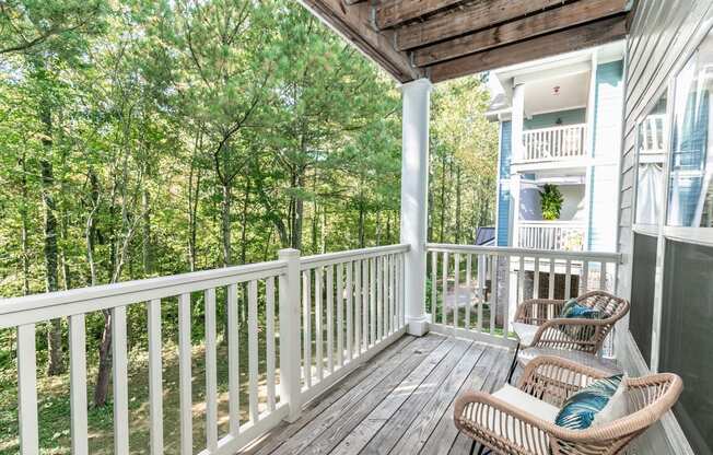 a porch with two wicker chairs and a view of trees