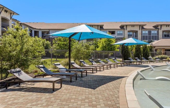A sunny day at the pool with blue umbrellas and lounge chairs.
