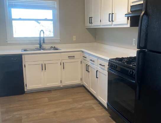 a kitchen with white cabinets and black appliances and a window