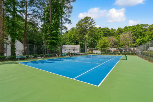 a tennis court with blue and green turf and a fence and trees