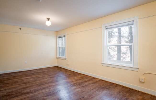 a bedroom with hardwood floors and two windows