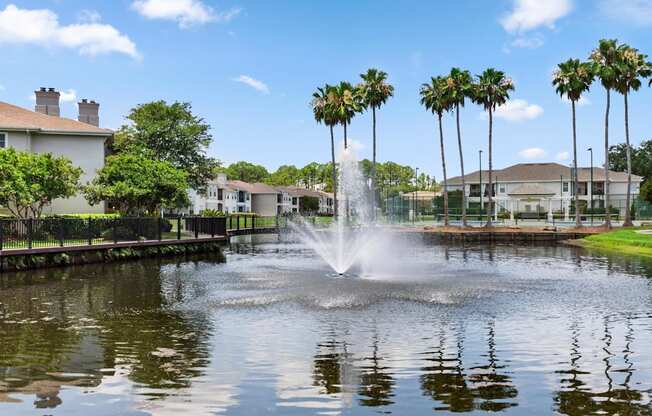 A fountain in the middle of a pond surrounded by palm trees.
