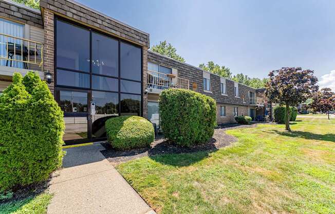 A building with a glass facade is surrounded by green bushes and trees.