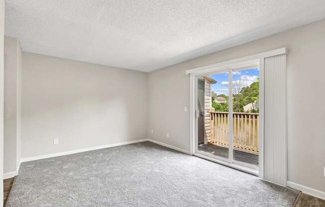 A room with a carpeted floor and a sliding glass door leading to a balcony.