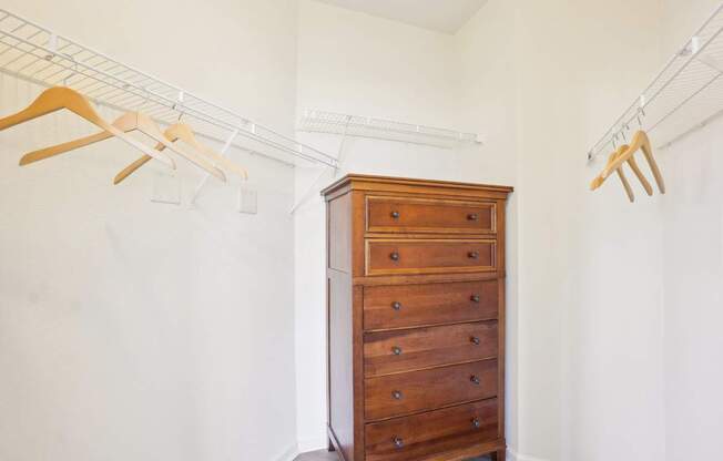 A wooden chest of drawers with clothes hanging on a rail above it.