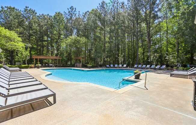 A pool surrounded by trees and lounge chairs.