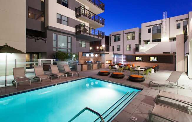 a swimming pool with lounge chairs and tables in front of an apartment building