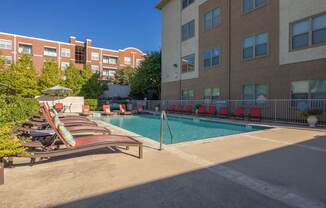 A pool area with chairs and umbrellas in front of a building.
