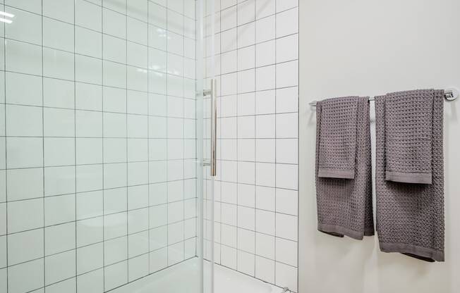 a white tiled bathroom with two towels hanging on the wall at Slabtown Square Apartments, Portland