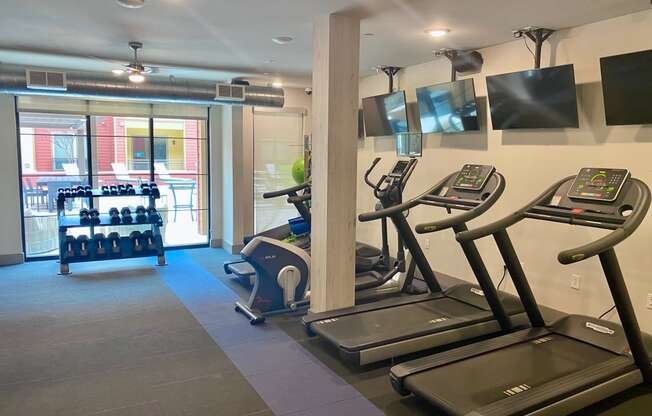 a gym with cardio machines and televisions on the wall