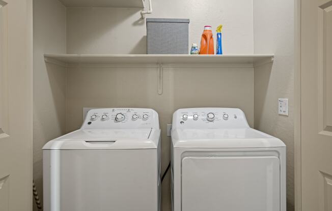 two washers and dryers in a laundry room with a shelf above them