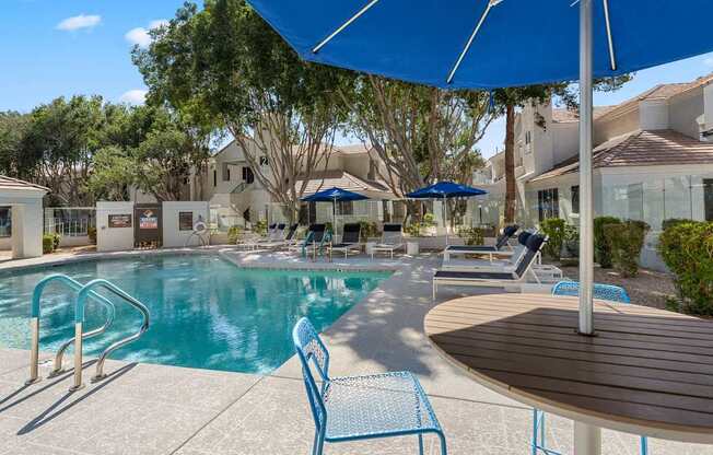 A pool area with a blue umbrella and chairs.