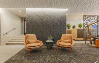 Two tan chairs are placed in front of a grey wall.