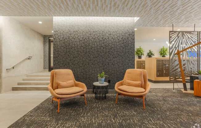 Two tan chairs are placed in front of a grey wall.