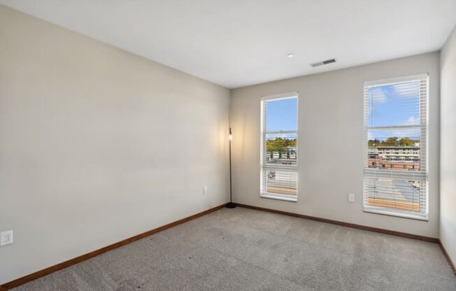 the living room of an apartment with two windows and a carpet