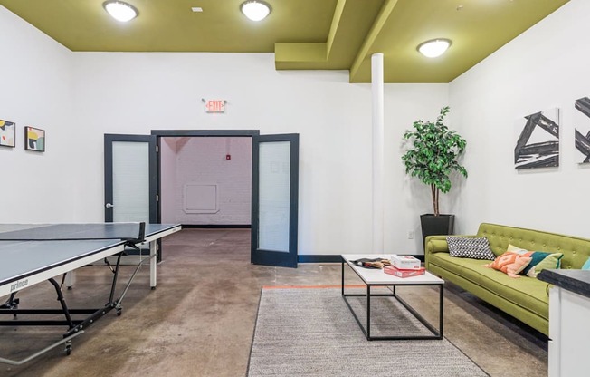 A room with a ping pong table and a green couch.