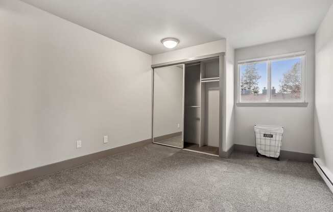 A room with a grey carpet and a white wall with a window and a trash bin.