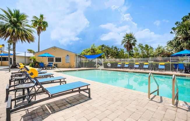 A pool area with sun loungers and a yellow building in the background.