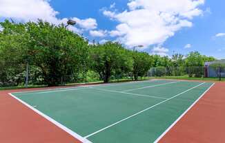 a tennis court with trees and a blue sky with clouds