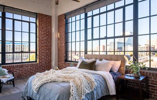 a bedroom with large windows and a bed with a blanket and pillows at The 22 Apartments, St. Louis, MO 63103