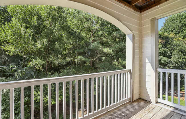 A balcony with a white railing and a view of a wooded area.