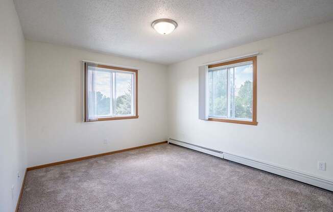 A room with two windows and carpeted floor. Bismarck, ND Sierra Ridge Apartments
