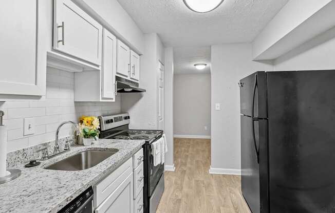 A black refrigerator is on the right in a kitchen with white cabinets.
