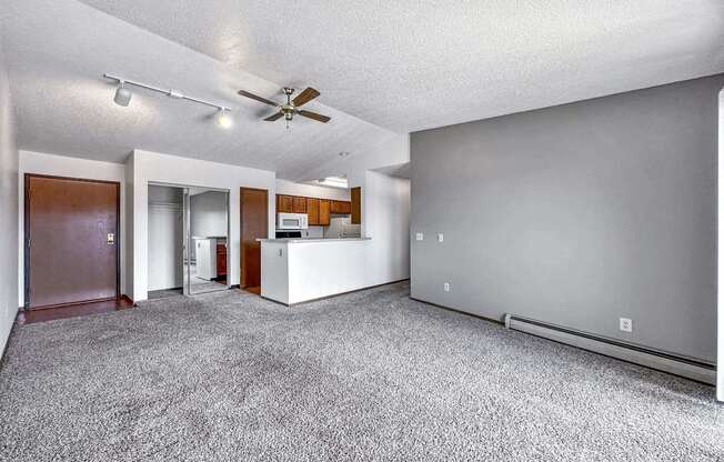 an empty living room with a ceiling fan and a kitchen