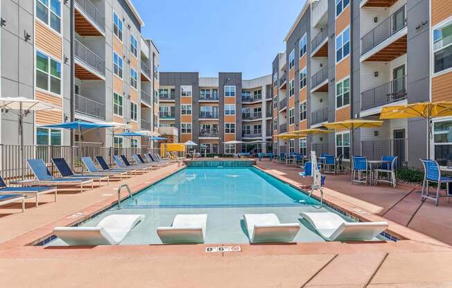 a swimming pool with chaise lounge chairs and umbrellas in front of an apartment building